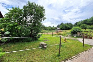 Um jardim com uma árvore grande, uma pedra e uma pequena construção.