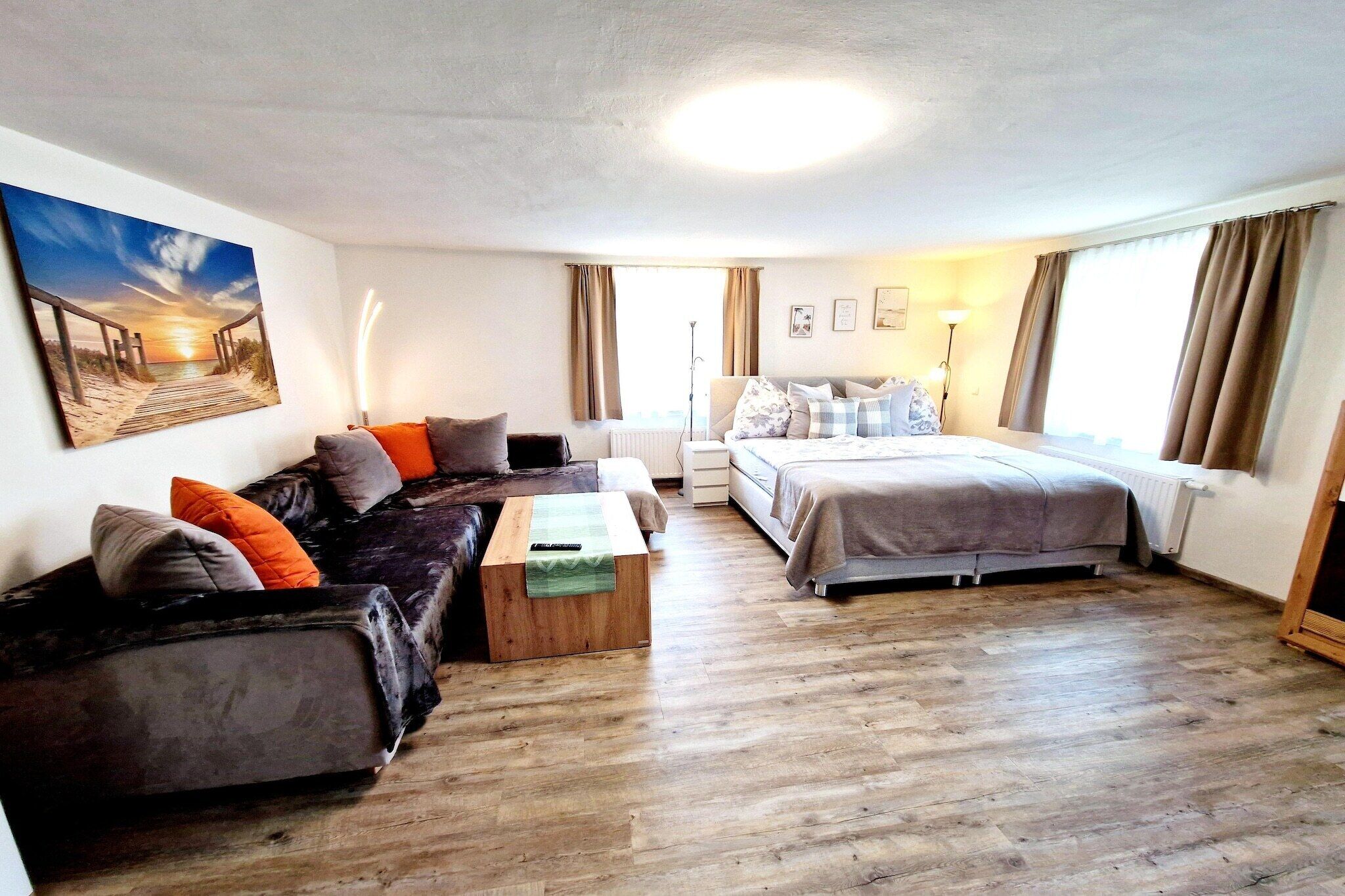 A room with a sofa, a bed, a wooden coffee table, and a painting on the wall.