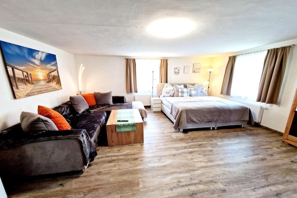 Une pièce comprenant un canapé, un lit, une table basse en bois et un tableau accroché au mur.