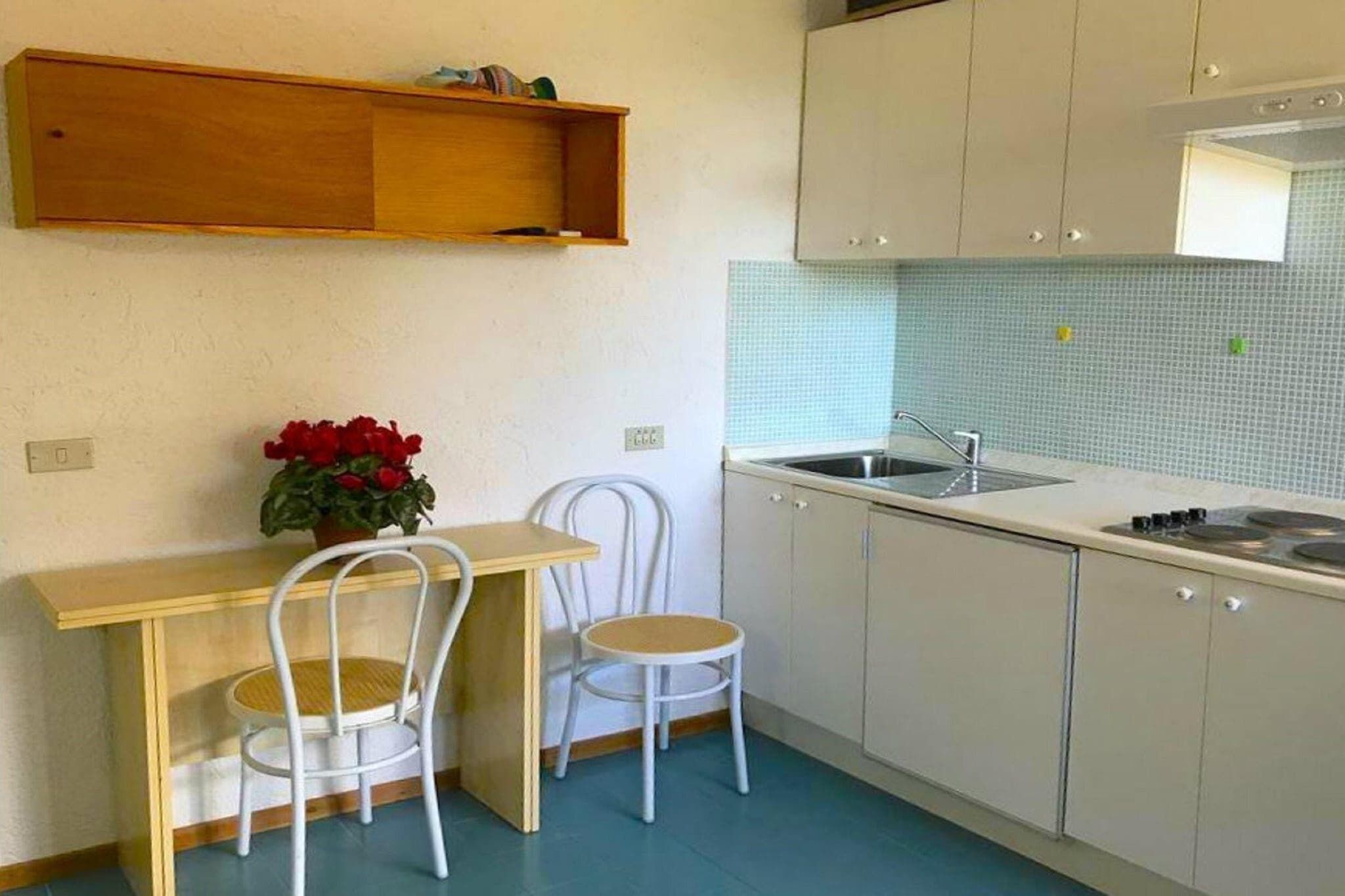 Uma cozinha compacta com bancada de madeira, duas cadeiras brancas, uma pia e painel de azulejos.