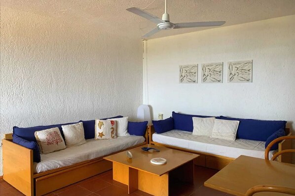 A room with two sofas, a ceiling fan, and three wall-mounted artworks.