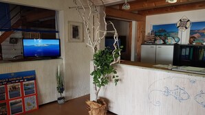A reception area with a wooden desk, a television displaying a scenic view, a potted plant, and a wall with nautical-themed decorations.
