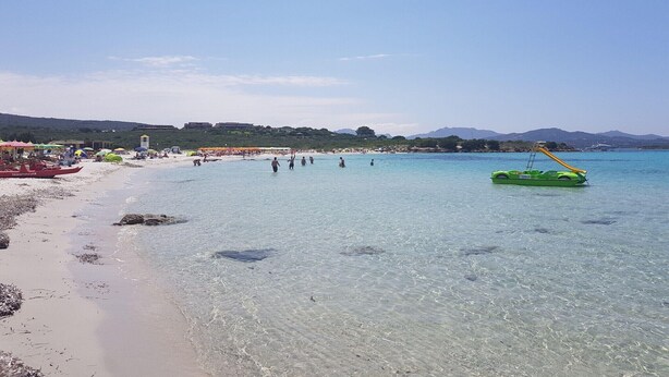 A beach with clear water, a sandy shore, and a few people.
