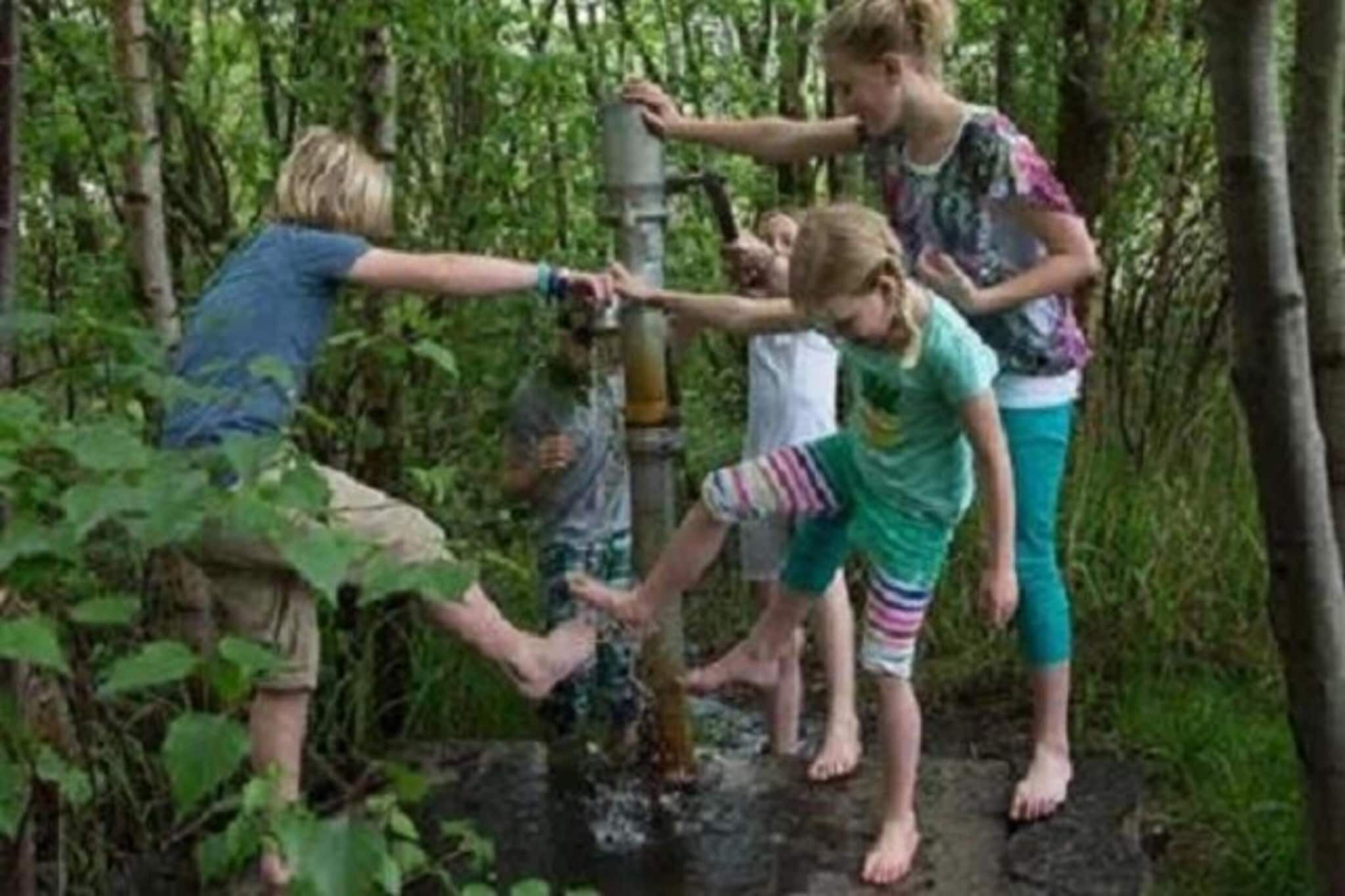 A group of people interacting with a water pump in a forested area.
