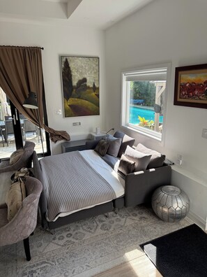 Un dormitorio moderno con una cama grande, vista a una piscina y un área de comedor visible a través de la ventana.