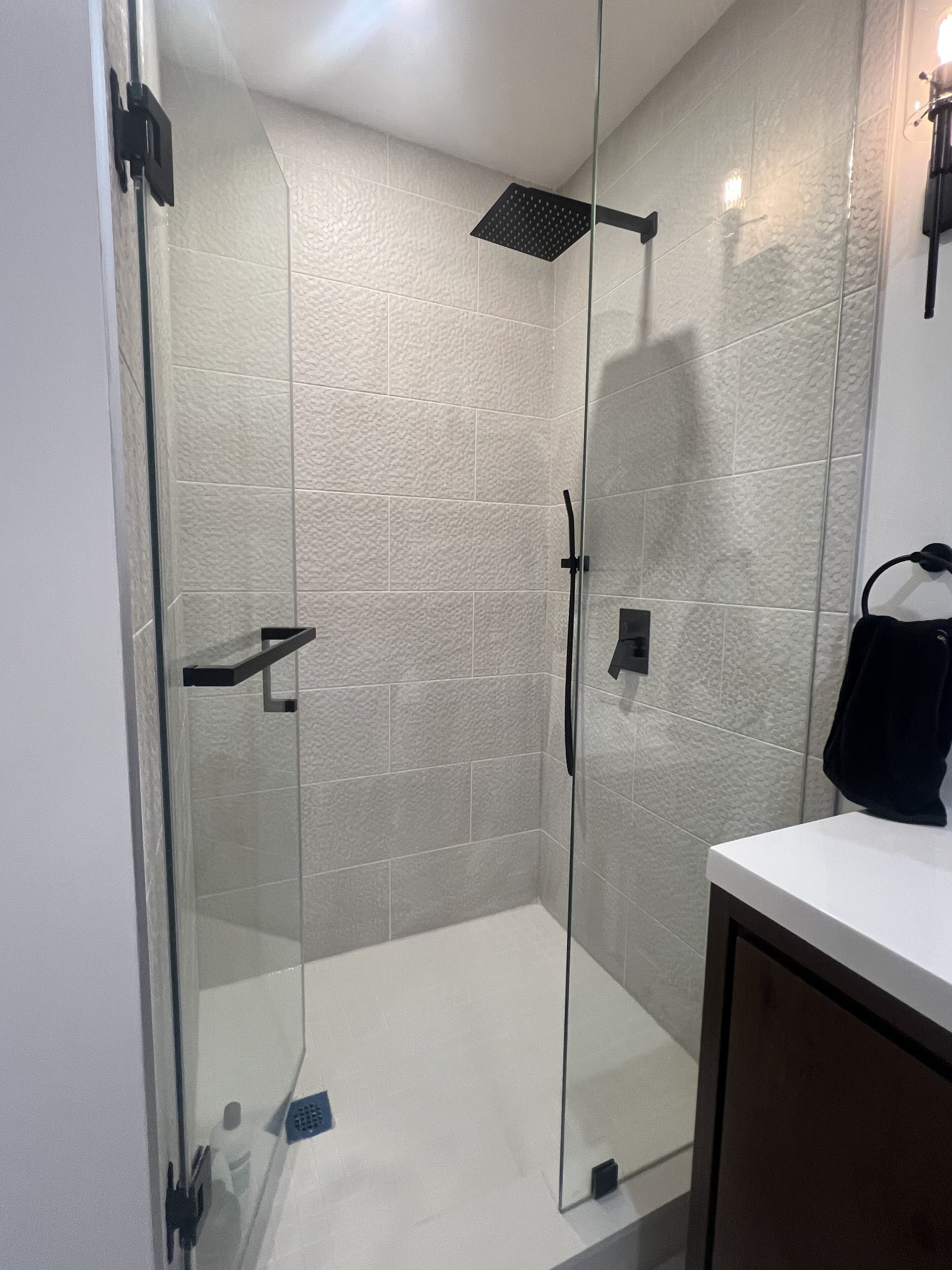A glass-enclosed shower with a black showerhead and a white tiled wall.