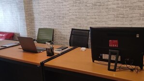 Ein Konferenzraum mit Backsteinwand, einem Holztisch, einem Laptop, einem Projektor und einer roten Couch im Hintergrund.