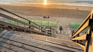 Una scala di legno che conduce a una spiaggia con un tramonto sullo sfondo.