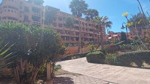 Ein Hotel mit einem gewundenen Weg, Palmen und einem großzügigen Gebäude mit mehreren Balkonen.