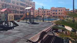 Ein Spielplatz mit Rutsche und Klettergerüsten, umgeben von einem befestigten Bereich und einem Zaun.