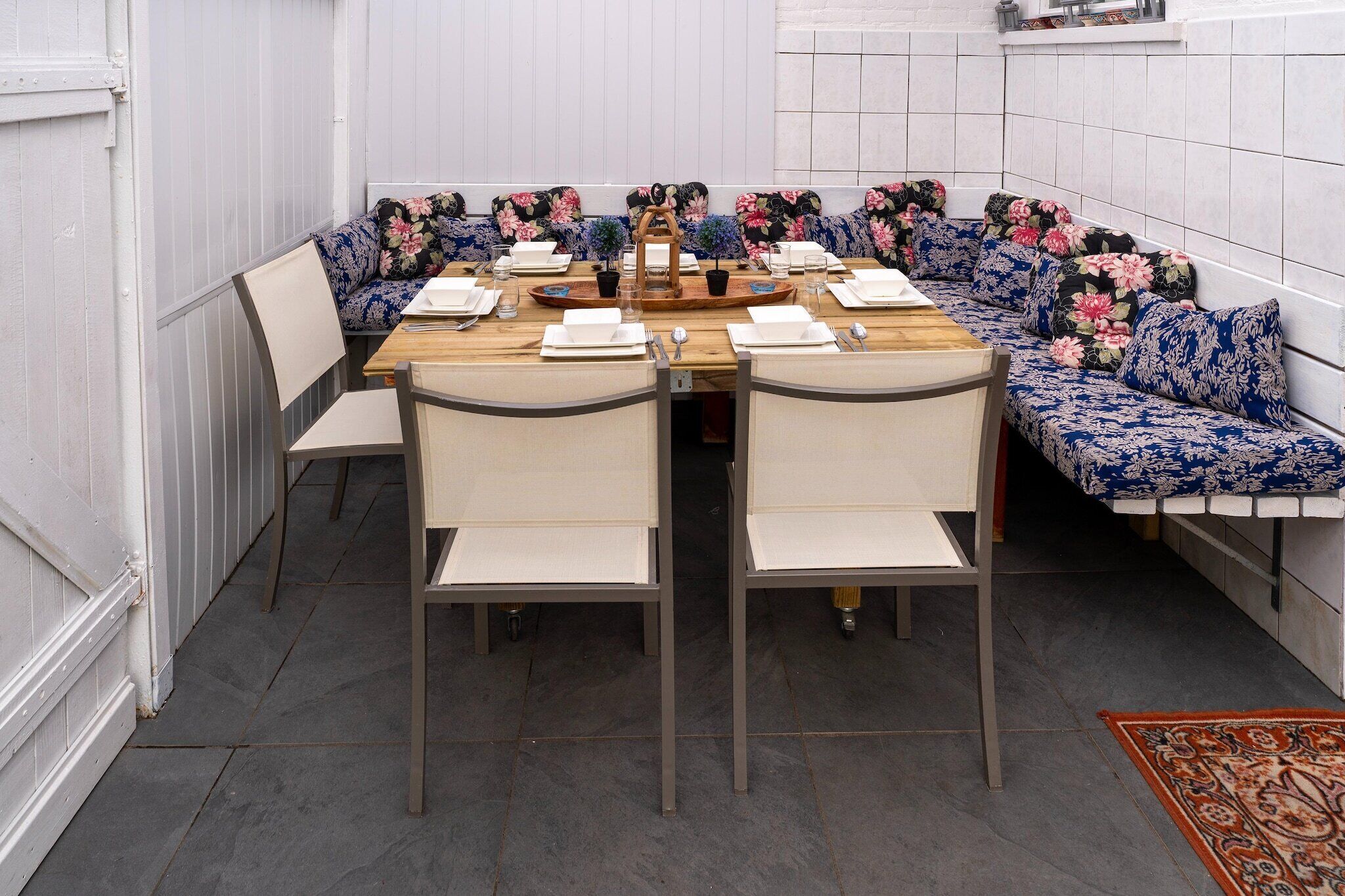 Uma sala de jantar com uma mesa comprida posta para seis pessoas, rodeada por sofás e cadeiras com estampa floral.