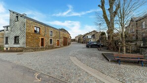 A cobblestone street lined with historic stone buildings, a parked car, and a bench. - Holiday home Les Hirondelle for 8 persons (Bievre)