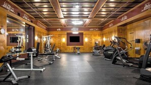 A gym with various exercise equipment, a large mirror, and a television screen on the wall. - CozySuites at The Block (Indianapolis)