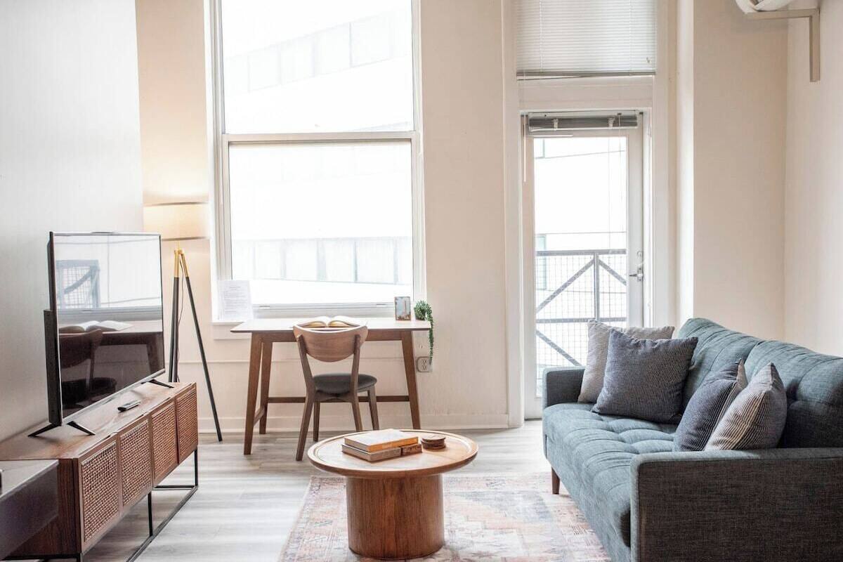 A modern living room with a sofa, a TV, a dining table with chairs, and a window with a view.