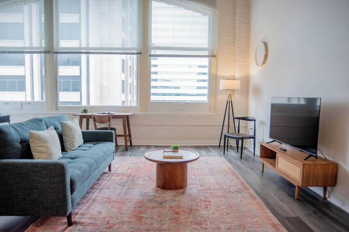 A living room with a sofa, coffee table, TV, and large windows.