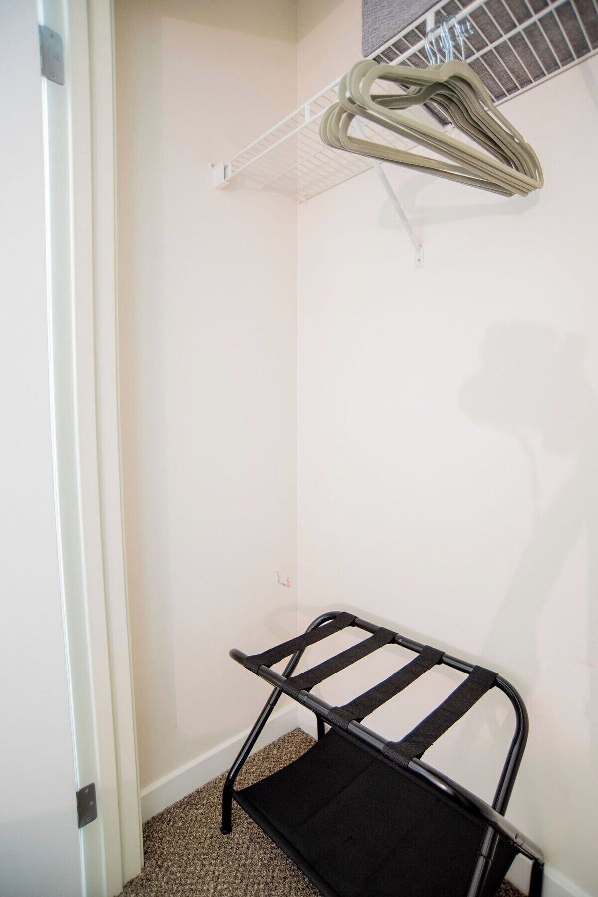 A small, narrow room with a black metal bench, a white door, and a clothes rack with hangers.