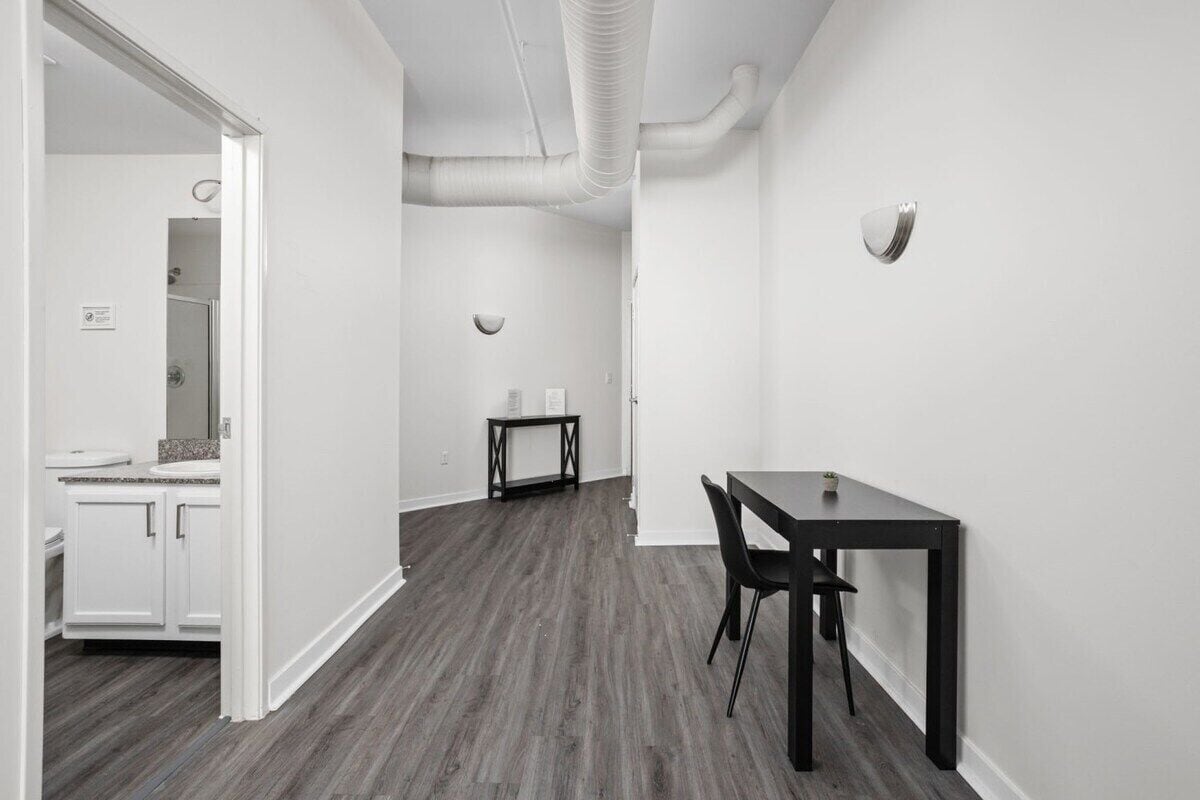 A modern kitchen with white cabinets, a dark wooden floor, and a dining area with a table and chairs.