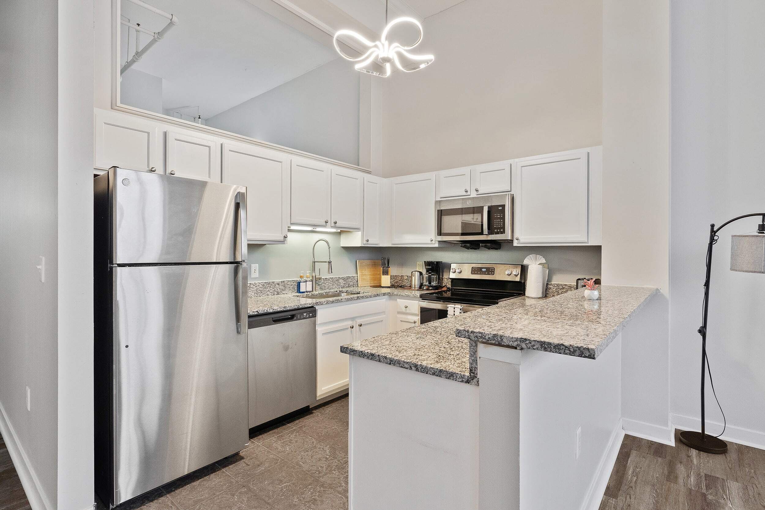 A modern kitchen with white cabinets, stainless steel appliances, granite countertops, and a pendant light.