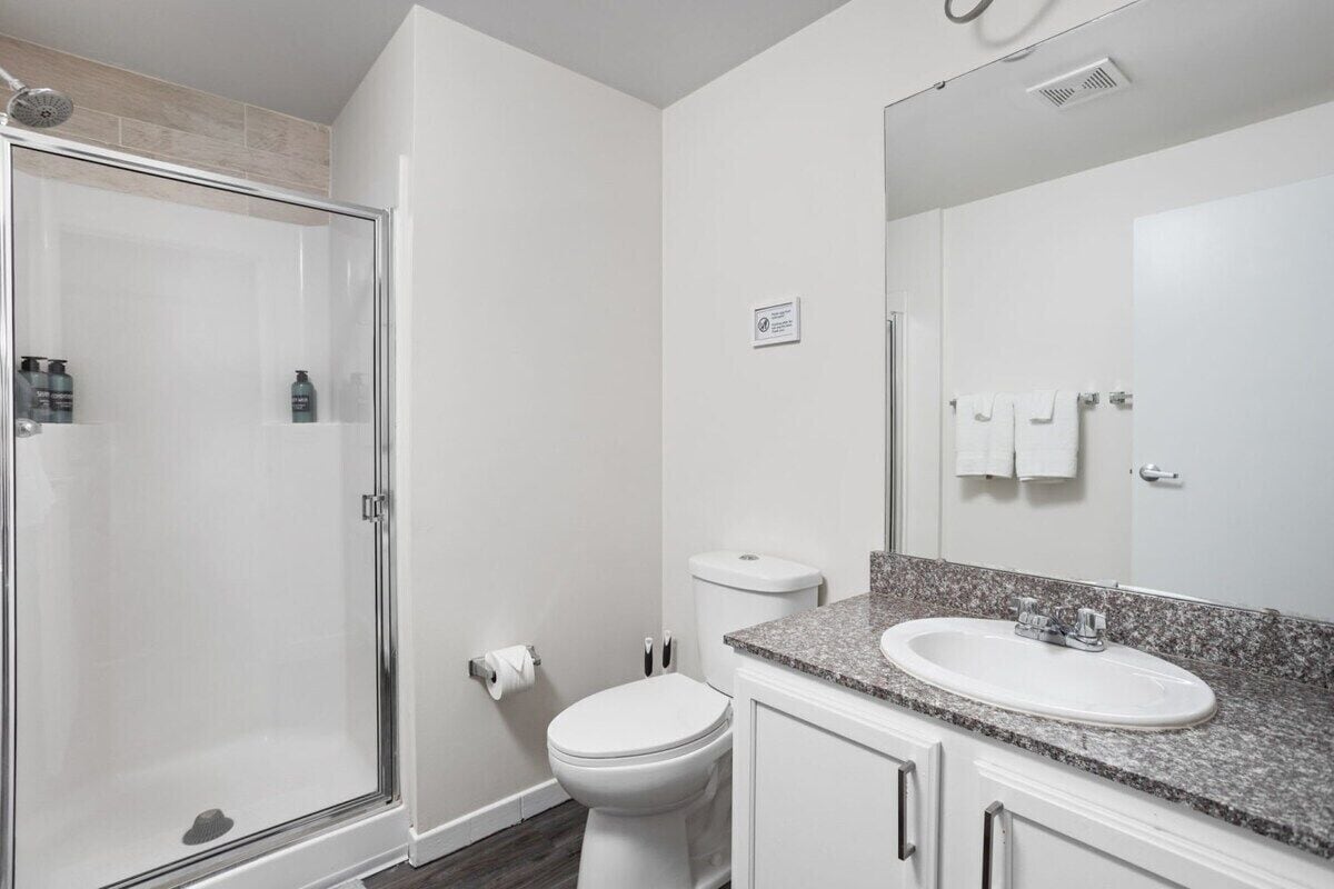 A bathroom with a shower, toilet, sink, and mirror.