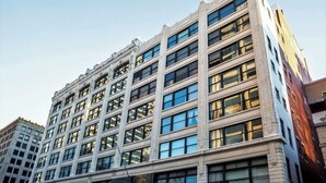 A multi-story building with a classical architectural style, featuring a symmetrical facade with evenly spaced windows and decorative elements. - CozySuites at The Block (Indianapolis)