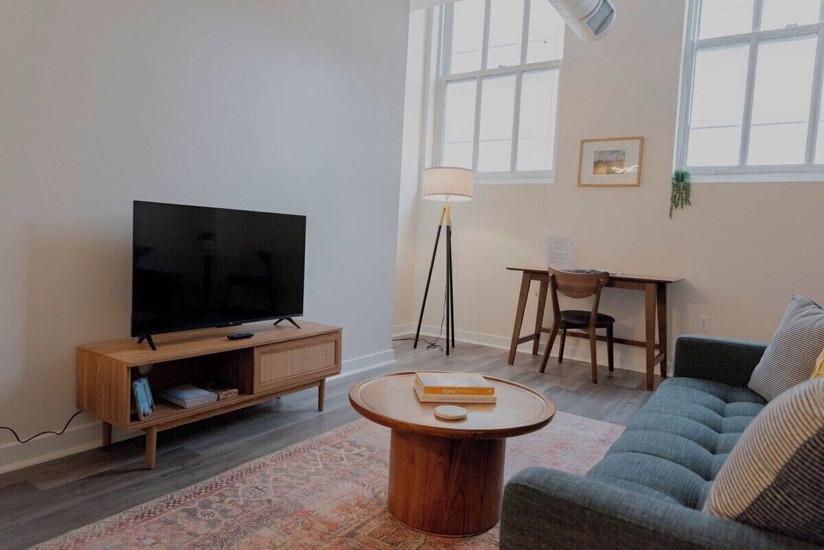 A living room with a TV, wooden entertainment unit, round coffee table, sofa, and a desk with chair.