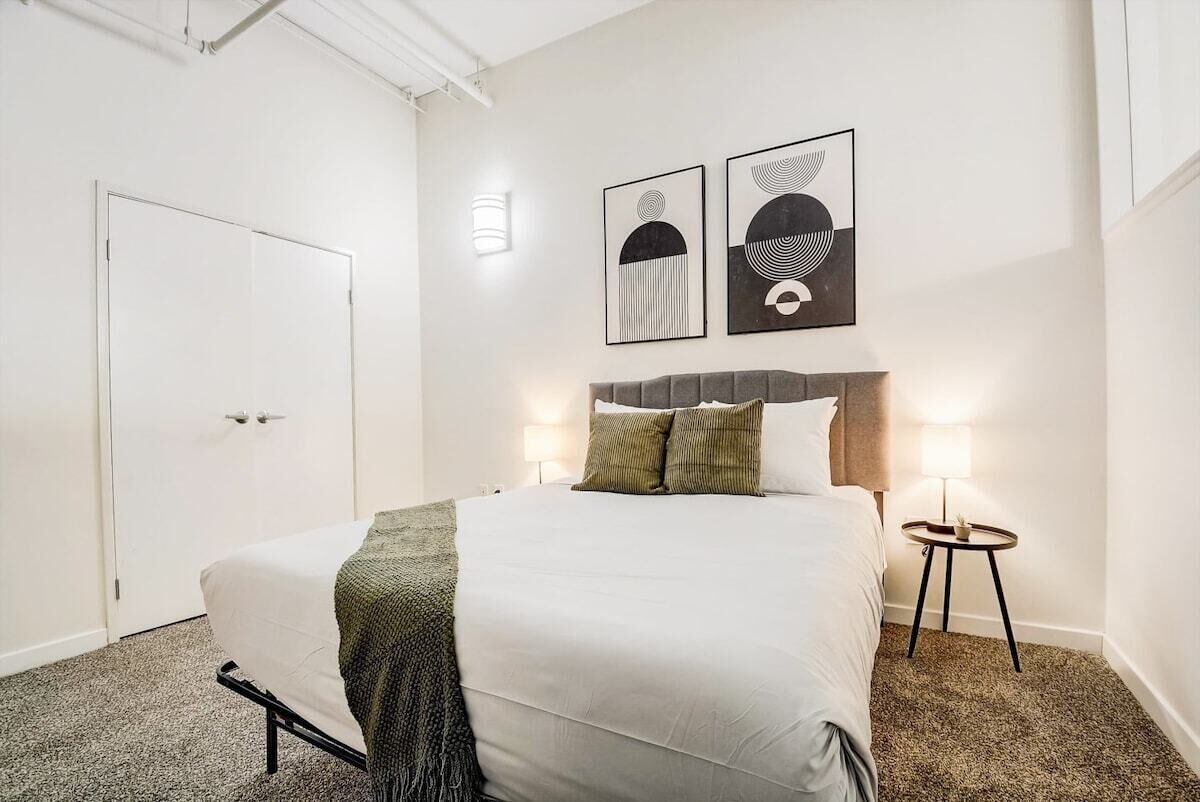 A bedroom with a bed, a bedside table, a lamp, and two framed artworks on the wall.