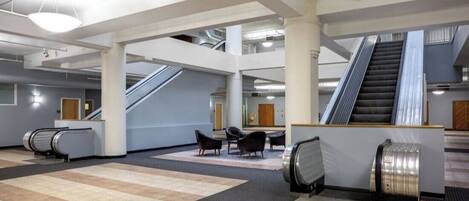 A spacious lobby with escalators, seating areas, and a modern architectural design.