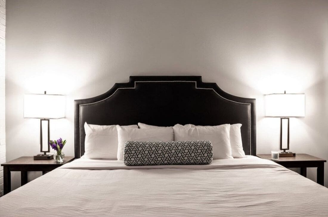Habitación de hotel con una cama grande, dos mesitas de noche y una mesita auxiliar con una lámpara y un florero.