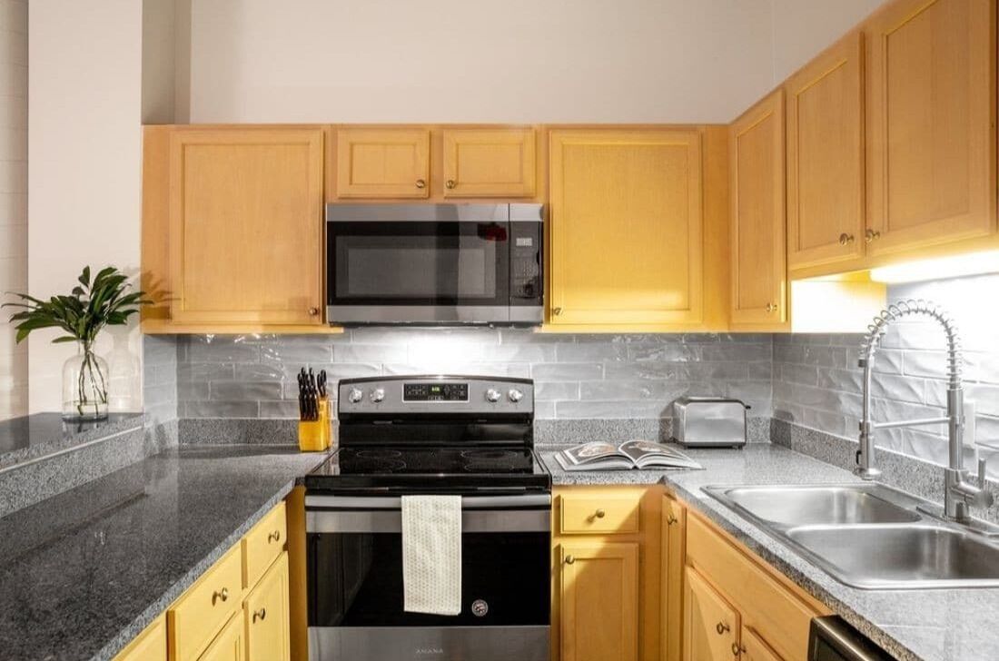 A kitchen with wooden cabinets, a microwave, a stove, a sink, and a toaster.