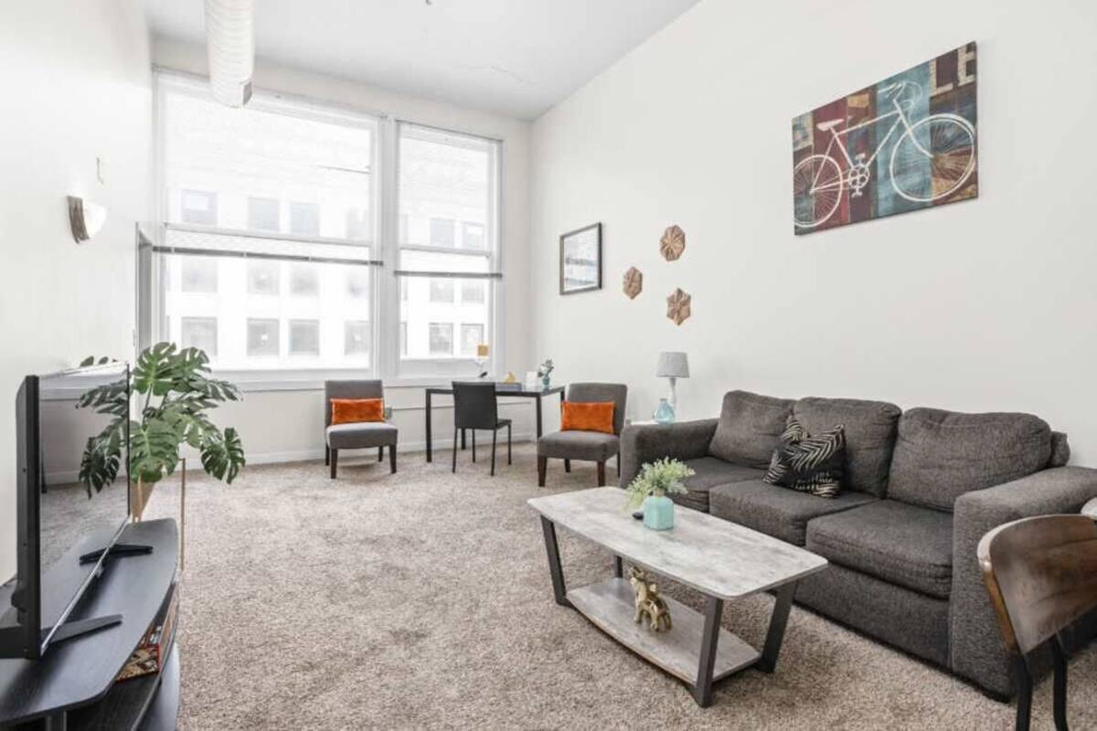 A modern living room with a grey sofa, a coffee table, a TV, and a large window.