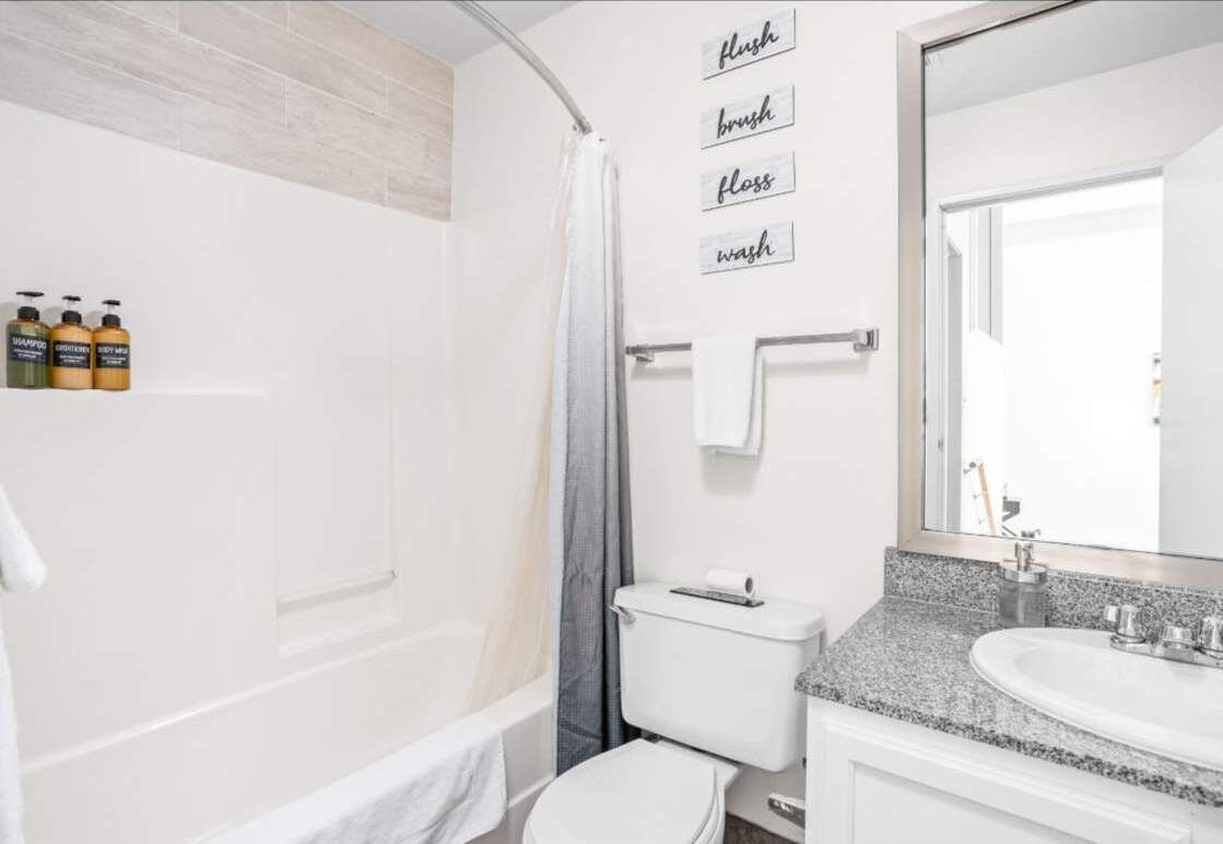 Ein Badezimmer mit Dusche, Toilette, Waschbecken und Spiegel. An der Wand befinden sich Pflegeprodukte und ein Handtuchhalter.