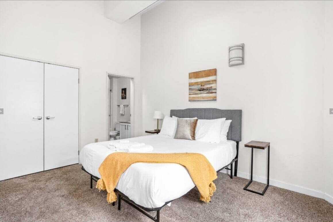 Un dormitorio con cama, mesita de noche, luz empotrada en la pared y una puerta.