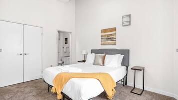 Un dormitorio con cama, mesita de noche, luz empotrada en la pared y una puerta.