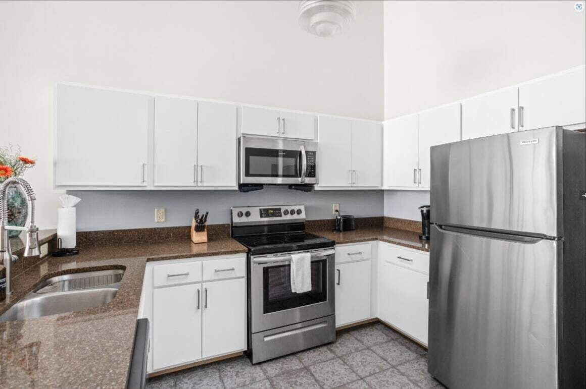 A modern kitchen with white cabinets, a stainless steel refrigerator, a microwave, and an oven.