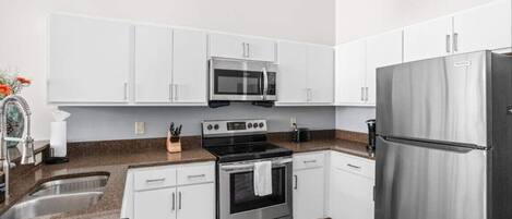 A modern kitchen with white cabinets, a stainless steel refrigerator, a microwave, and an oven.