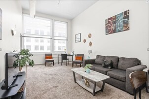 Una sala moderna con un sofá gris, una mesa de centro, un televisor y un ventanal grande.