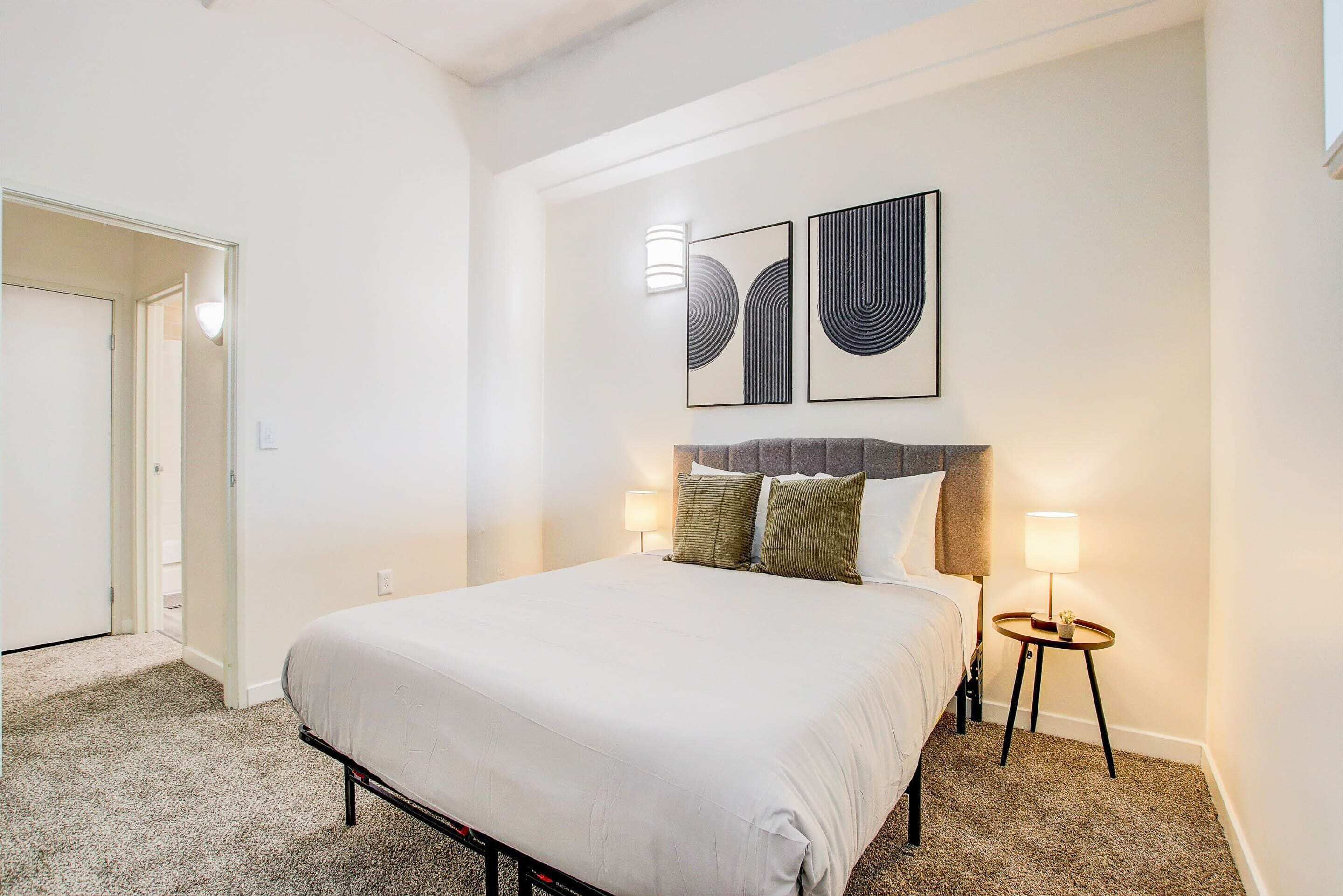Una habitación de hotel con una cama, dos mesitas de noche con lámparas y arte abstracto en la pared.