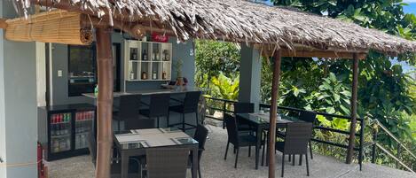 An outdoor seating area with a thatched roof, a bar with liquor bottles, and wicker furniture.