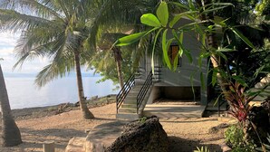 Une propriété située en bord de mer, avec un escalier menant à un bâtiment, entourée de palmiers et bordée d’une côte rocheuse.