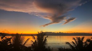 Un coucher de soleil sur une étendue d’eau calme, avec des silhouettes de palmiers au premier plan.