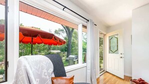 A modern living room with a large window, a grey sofa, a red umbrella, and a wicker basket.