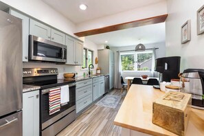 A modern kitchen with stainless steel appliances, a wooden island, and a view of the outdoors. - Urban Gem: Mins to Beach & Downtown + Hot tub! (Traverse City)