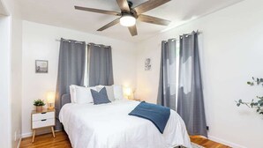 A bedroom with a bed, a nightstand, a ceiling fan, and curtains.