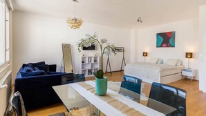 Un salon moderne avec une table à manger en verre, un canapé et un lit doté d’une tête de lit blanche.