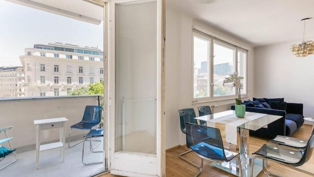 Un balcon ouvert avec un coin repas, un canapé et une vue sur les bâtiments de la ville.