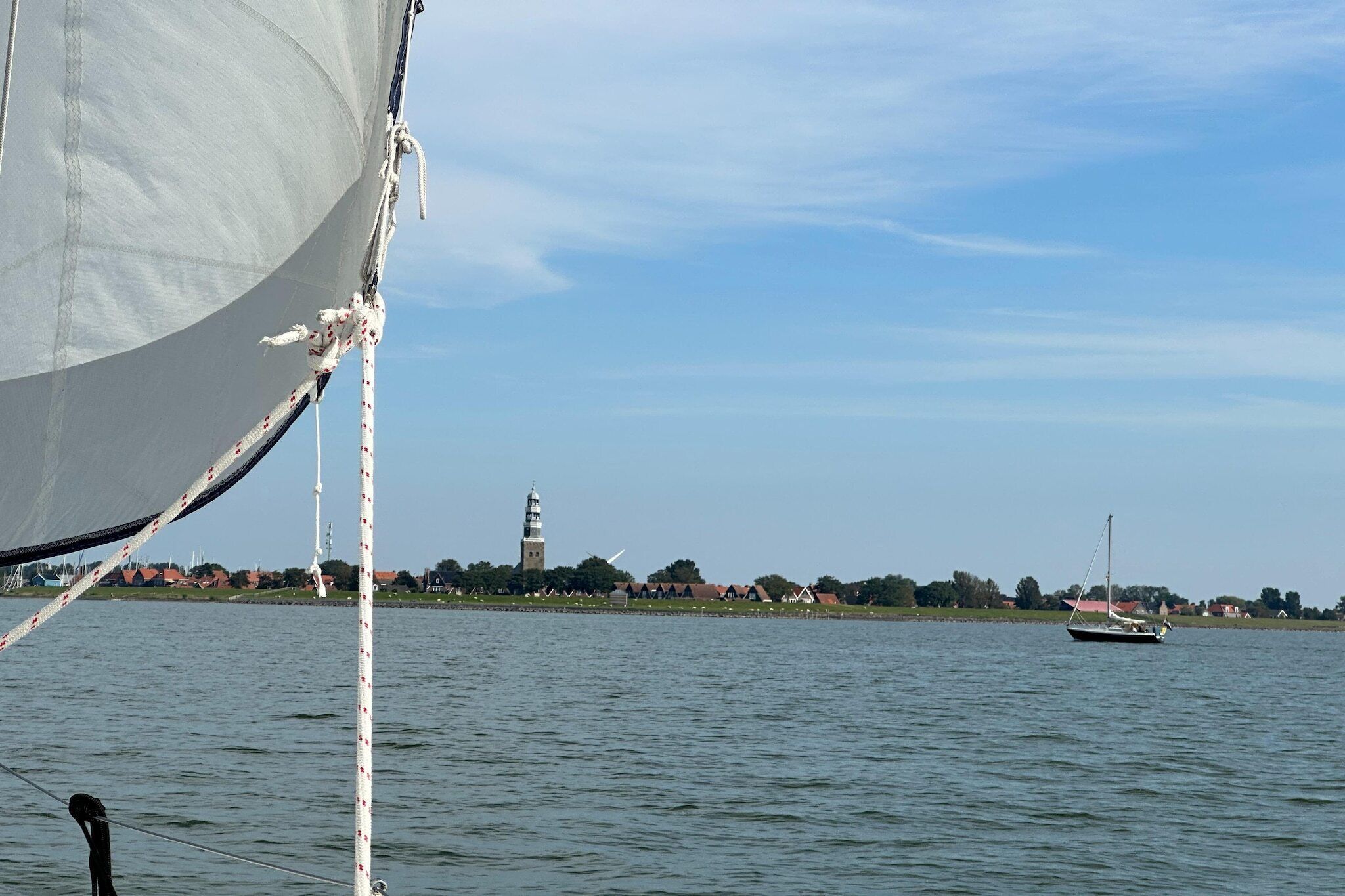 A sailboat on calm waters with a distant view of a town and a tower.