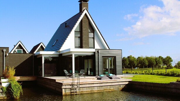 Ein modernes Haus mit Satteldach, großen Fenstern und einem Steg, der ins Wasser führt.