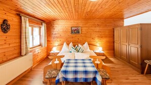 Ein gemütliches Holzhütten-Zimmer mit Bett, Tisch mit Stühlen, einem Fenster mit Vorhängen und einem Kleiderschrank.