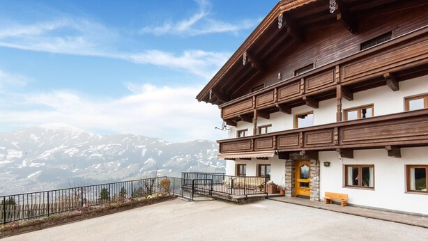 Ein zweistöckiges Gebäude mit Holzfassade, einem Balkon und Blick auf schneebedeckte Berge.