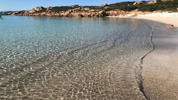 A clear beach with rocky outcrops and a boat in the water.
